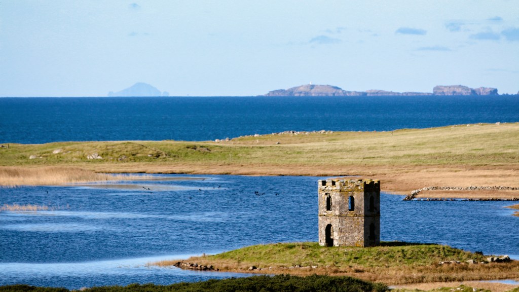 A photo from North Uist looking out across a lochan with an island fort towards St. Kilda. 